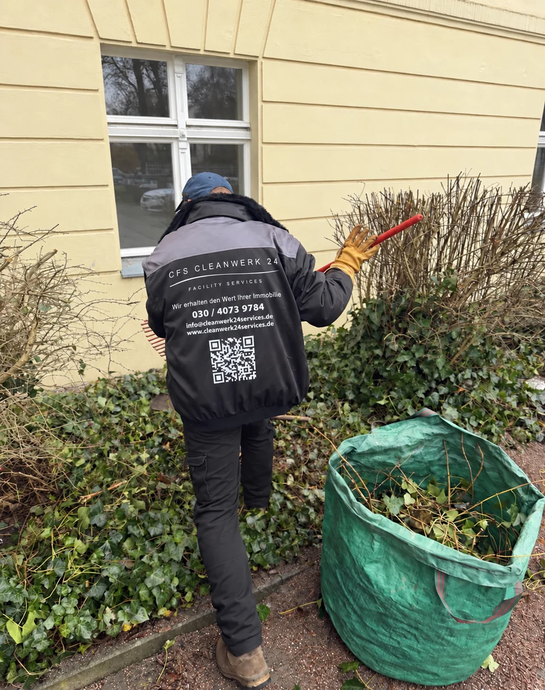 Mitarbeiter in Arbeitskleidung von CFS Cleanwerk24 Facility Services bei der Heckenpflege vor einem Gebäude