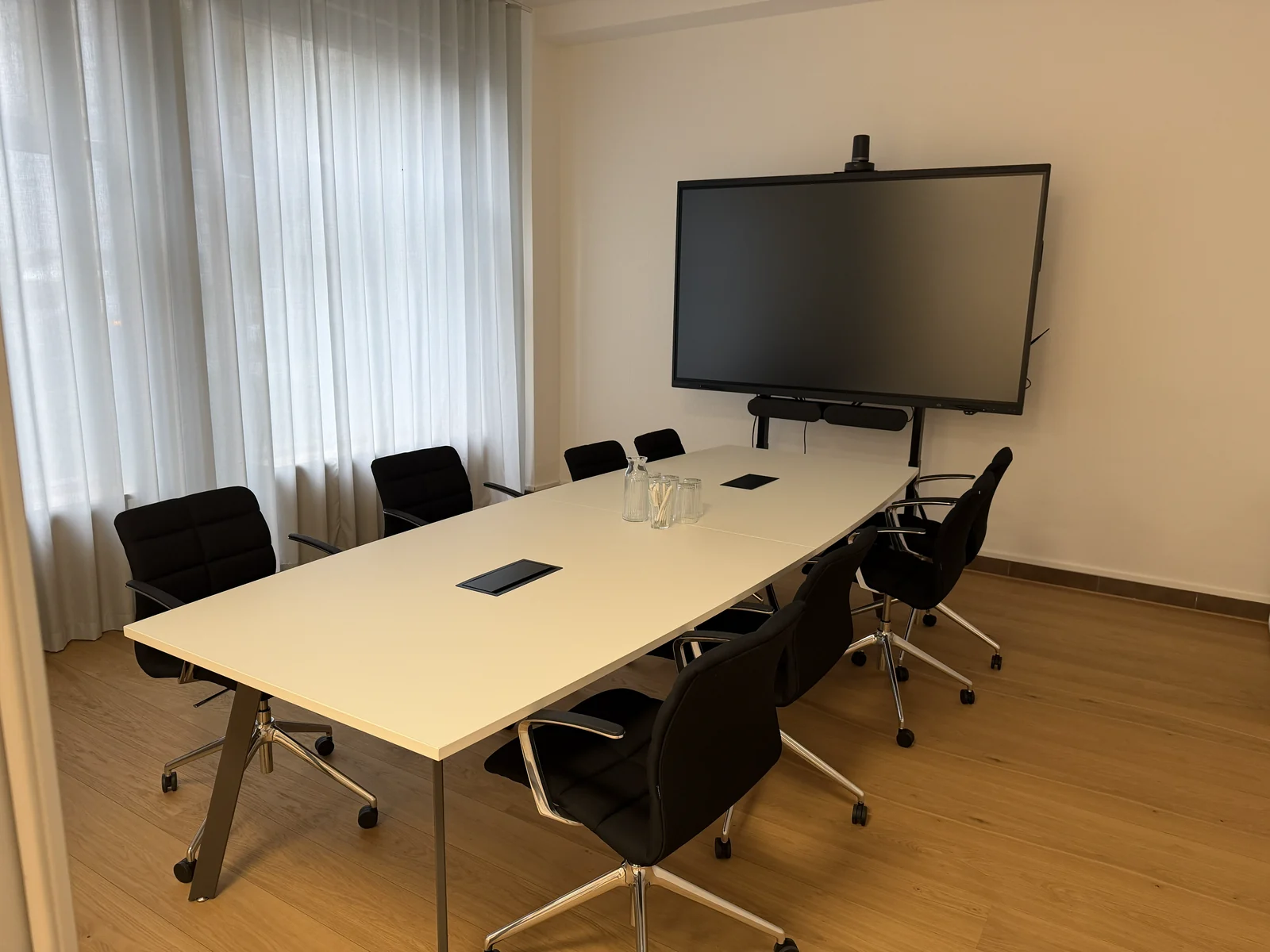 Well-kept meeting room with a conference table, black office chairs and a screen
